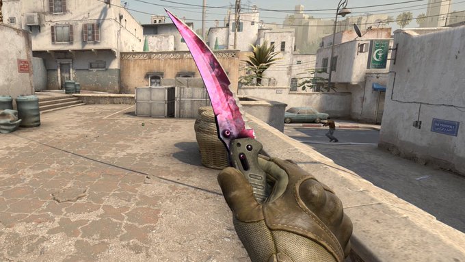 A first-person view shows a hand wearing a tactical glove holding a vibrant pink and purple knife skin in the game Counter-Strike, set against a sunny desert map environment. The flashy, aggressive weapon skin paired with the confident pose perfectly captures the cocky, bullish energy of someone ready to dominate the next crypto market rally.