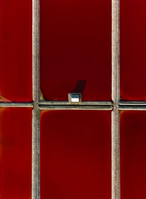 A close-up of a small metal object, possibly a razor blade or scraper, positioned behind the bars of a red window or grate.