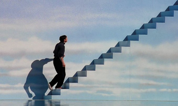 An artistic image of a man in black clothing climbing blue stairs that ascend into a cloudy sky, casting a shadow against the backdrop.