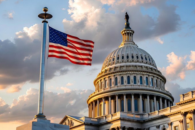 The US Capitol Building dome is shown against a cloudy sky at sunset, with an American flag waving on a flagpole in the foreground.