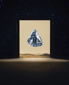 A stylized image showing a floating, crystalline triangular shape framed by a doorway against a backdrop of desert dunes and a starry night sky.