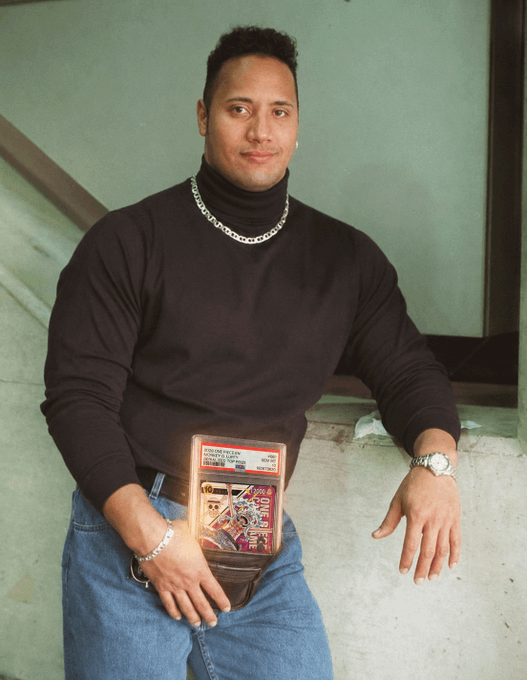 A man poses holding a Collector Edition Ultra Rare 56kpack card, wearing a black turtleneck with silver chain and watch, smiling in front of a greenish wall — fitting the caption's tease about pulling the rare Gear 5 Luffy card with "signs" being his confident, watchful pose.