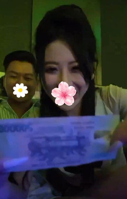 A photo of two people with flower emojis covering parts of their faces, where one holds a glowing purple item in a dimly lit setting.