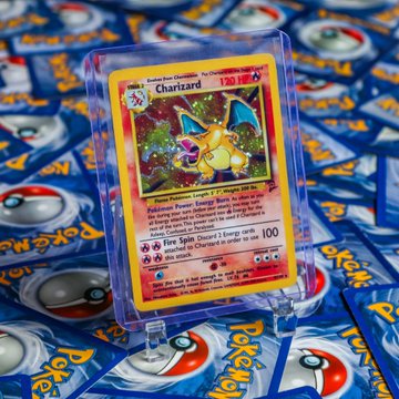 A holographic Charizard Pokémon card (120 HP, Fire Spin ability) sits prominently atop a stack of Pokémon card packs. The image visually reinforces the post's claim about Pokémon cards outperforming Bitcoin, showcasing a rare collectible card as a symbol of the booming Pokémon market.