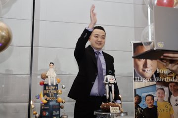 Shohei Ohtani in a suit waves beside birthday cakes decorated with his bobblehead figure, with a 'Happy Birthday' book featuring him on the right.