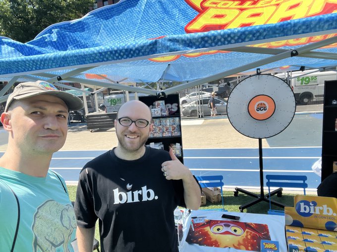 Two men smile for the camera at an outdoor event under a blue tent; one wears a black 'birb.' t-shirt, and a sign reading 'PHILADELPHIA PARKS' is visible.
