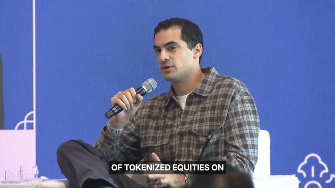 A man in a plaid shirt speaks into a microphone during a panel discussion, with on-screen subtitles reading 'OF TOKENIZED EQUITIES ON'.