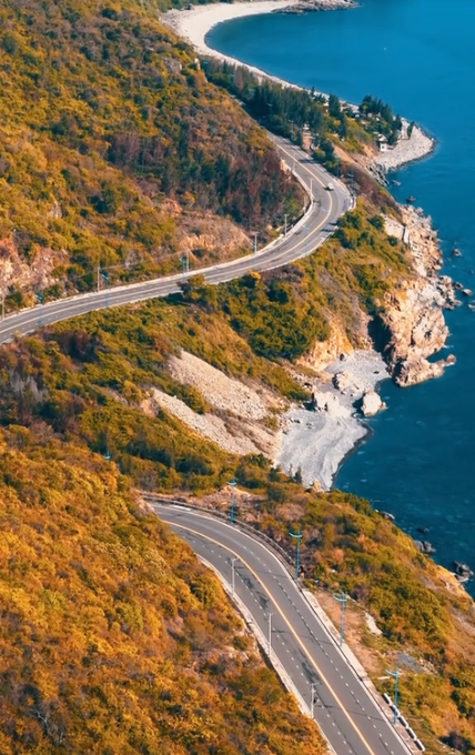 A scenic aerial view of a winding coastal road hugging the cliffs beside a turquoise sea, evoking the journey and perseverance behind the "grinding YAP" mentioned in the post.