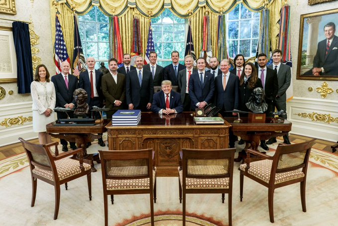 A group photograph in the Oval Office showing President Donald Trump seated at the Resolute Desk surrounded by members of his cabinet and administration, with a portrait of Ronald Reagan visible on the right wall.