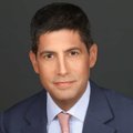 A professional headshot of a dark-haired man in a dark suit, white shirt, and pink tie is shown against a dark background. The image appears to be a profile photo of the financial analyst or commentator who is providing the cautionary technical analysis on the $SPX chart.