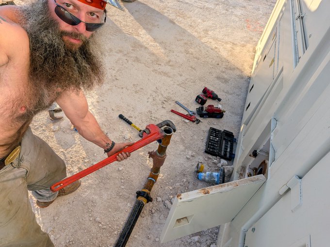 The image shows a bearded man wearing sunglasses holding a red pipe wrench while working on a project outside. The scene appears to be related to an electrical or plumbing issue, as there are tools scattered around him. A water bottle can also be seen nearby. The context of the image suggests that it might be a weekend when people have more free time for home improvement projects or repairs.

The post seems to be a humorous commentary on the situation, with the man's actions and the presence of various tools indicating an attempt to fix something at home. It appears that the man is trying to tackle a problem related to energy consumption or infrastructure, possibly involving electrical wiring or plumbing issues. The image captures the essence of weekend DIY projects and the challenges they can present.