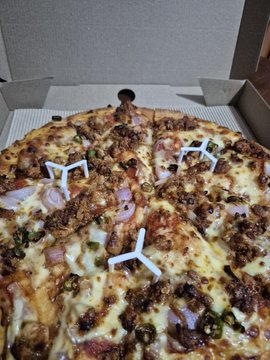 iced pizza with sausage, mushrooms, and onions on a white plate, resting on a wooden table.