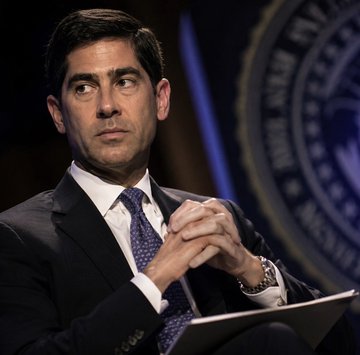 The image shows a serious-looking man in a dark suit and patterned blue tie, seated with his hands clasped in front of a partial blue seal that appears to read "BOARD OF GOVERNORS" — suggesting a Federal Reserve official. The post connects this to concerns about Kalshi prediction markets pricing in a higher likelihood of a September Fed rate hike, even as Bitcoin rallied, implying the Fed may be signaling tighter policy than markets expect.