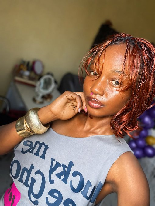 A young woman with red braids poses seriously with her hand near her chin, wearing a tank top reading "MY LUCKY [partially visible]". Her unsmiling expression matches the post's caption about not smiling until $ANSEM flips pumpfun.