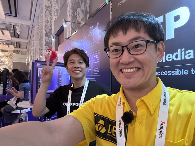 The image shows a selfie of two smiling men at what appears to be a trade show (Web3 Summit 2026, based on the lanyards), with one man holding up a peace sign and a small red plush toy, while text reading "NFT Media" is visible in the background. The post "Affinity too high case declared" humorously frames their close, friendly pose as evidence of an impossibly high "affinity" stat, playing on RPG/relationship terminology.