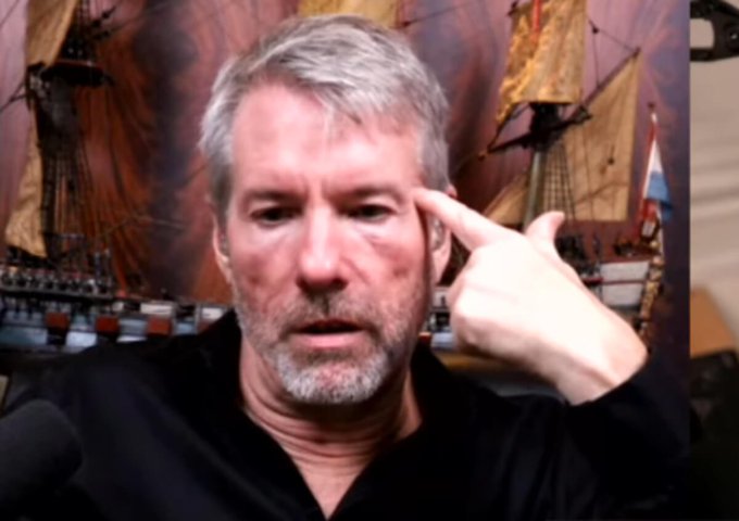 A gray-haired, bearded man in a black shirt points to his temple, appearing to make a thoughtful or exasperated gesture, set against a backdrop of model sailing ships. The image accompanies a post expressing frustration about Bitcoin's volatile price swings after hitting $100k, symbolizing the mental strain and second-guessing investors experience when their "never sell" conviction is tested by sudden market crashes.