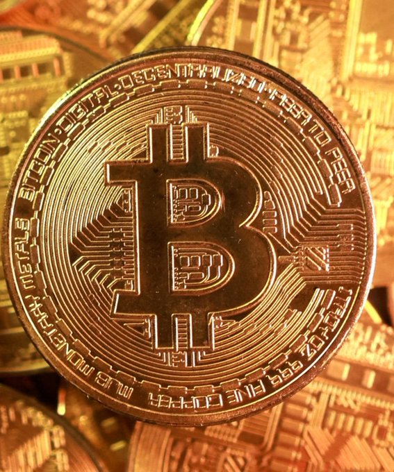 A copper-colored physical Bitcoin token rests on a pile of similar coins, with visible text reading "BITCOIN DIGITAL DECENTRALIZED PEER TO PEER" around the edge and "999 FINE COPPER MONETARY METALS" along the bottom. The image directly illustrates the post's discussion of Bitcoin's rally to $86,000, visually emphasizing the $BTC cryptocurrency at the center of investor rotation.