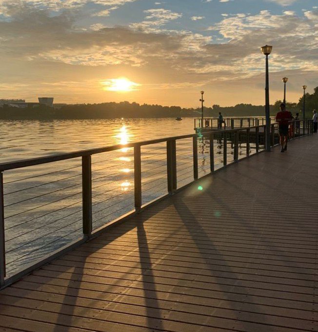 A serene sunrise casts a golden glow over a boardwalk with runners, symbolizing the daily grind and the potential for breakthroughs that come with perseverance.