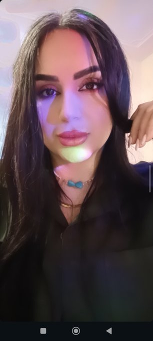 A young woman with long dark hair looking at the camera, with colorful lighting effects on her face.