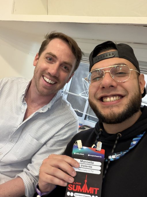 Two smiling men take a selfie at a Lunar Summit event, with one wearing a 'Morcello Volente' credentials badge from SUI.