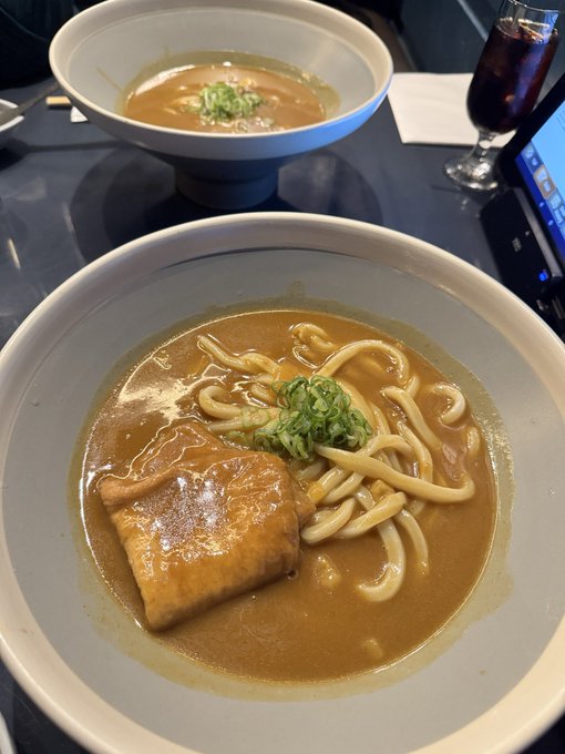 A bowl of Japanese curry udon with green onions next to a glass of iced cola.