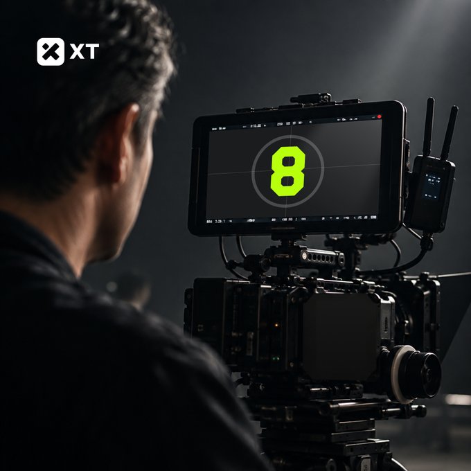 A person operates a professional video camera setup featuring a monitor displaying a large green number '8', with an 'XT' logo in the upper left corner.