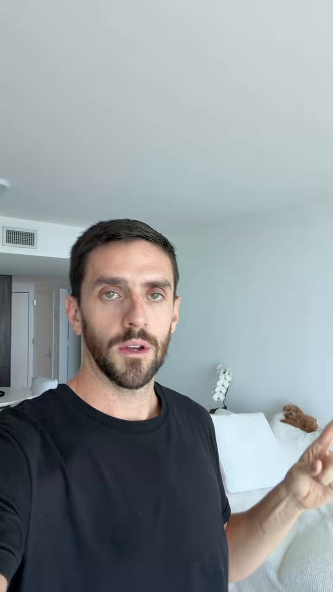The image features a man wearing a black shirt, standing in front of a bed with white pillows. He appears to be making a funny face or gesture for the camera while taking a selfie. The caption below the photo reads "Urgent Bitcoin and Crypto update". This suggests that there might have been some recent news or event related to cryptocurrency or Bitcoin that caught his attention, prompting him to take a selfie with this message displayed in the caption.