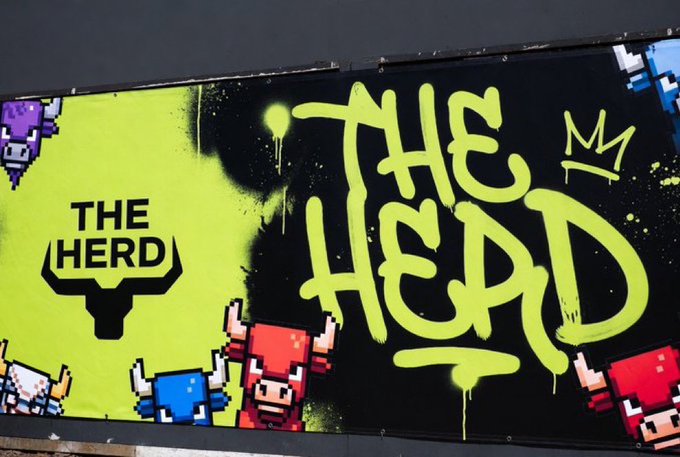 A billboard displays graffiti-style art reading 'THE HEAD' in bright yellow-green, accompanied by 'THE HERD' logo with a bull icon and pixelated bull and cow characters.