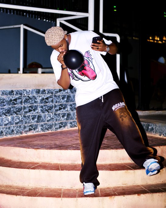 The image features a man wearing a white t-shirt with a black design of a lion's face and pink tongue, standing on some stairs while holding a black balloon. The background includes a brick wall and a chair, suggesting an indoor setting like a lounge or a party venue. The caption to the image reads "Most people don't think about security until something goes wrong. That's what makes $Quip and @quipnetwork stand out to me". This statement highlights the importance of considering security in various aspects of life, including social events where balloons might be present.

The man holding a balloon is likely capturing a memorable moment at an event or gathering by using his cell phone to take a photo. The image serves as a reminder that security should always be considered and prioritized, even when enjoying oneself in a relaxed setting like a lounge or party venue.