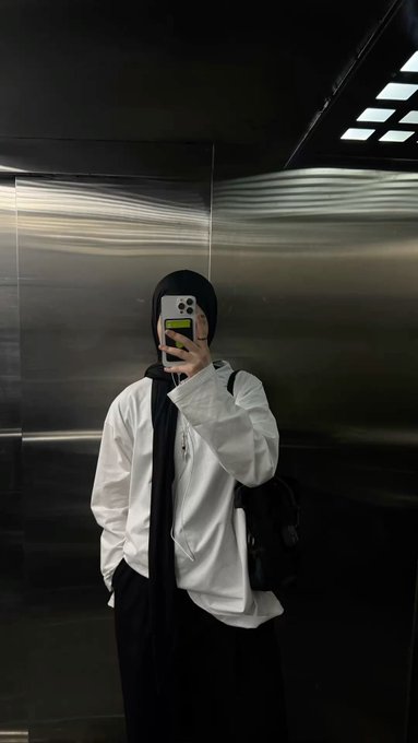 The image features a person wearing a white shirt, black pants, and a black headscarf taking a selfie with their phone. The background of the photo shows a metal wall or ceiling, which could be an elevator or a similar enclosed space. There is also text in the image that reads "Good night @quipnetwork use WOTS+ to add quantum-resistant security to Bitcoin assets". This suggests that the person might have been taking this selfie while attending a social event or gathering related to cryptocurrency and blockchain technology, possibly at an elevator where they were capturing the moment.

The main focus of the image is on the individual's face as they take their picture with their phone. The background serves as a contrast to the subject, making them stand out more prominently in the photo.