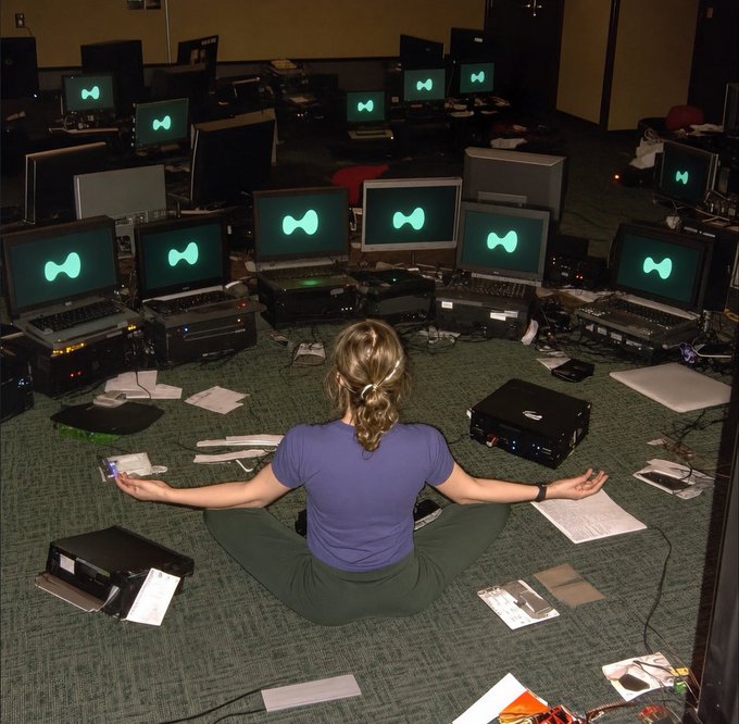 The image shows a woman sitting cross-legged on the floor, surrounded by multiple laptops and computer monitors. She appears to be engaged in some sort of activity or work related to technology. The scene also includes several books scattered around her, indicating that she might be researching or studying various topics. The post about Polymarket has been flipped upside down, which adds an element of surprise and humor to the image.