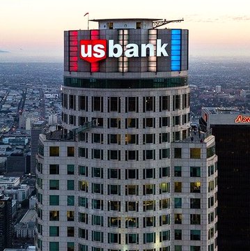 An aerial view of the U.S. Bank Tower in Los Angeles at dusk, with the illuminated "usbank" logo prominently displayed at the top of the building.