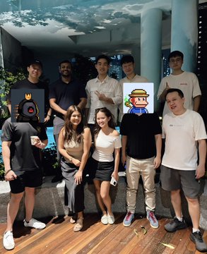 A group of nine people posing for a photo at night, with two individuals in the back wearing pixelated character masks.