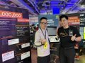 Two young men posing in front of a backdrop featuring the text 'LOGO1688' or similar at what appears to be a gaming or electronics exhibition booth.