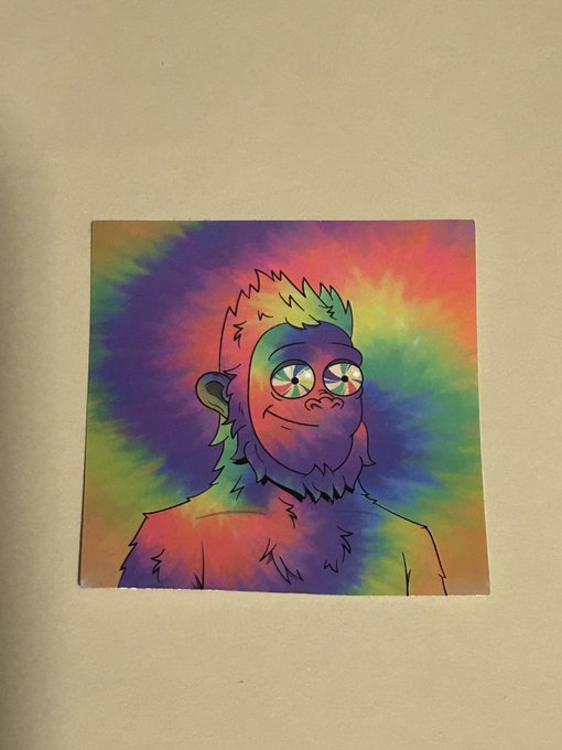 A small square sticker or print featuring a colorful tie-dye background with a cartoon drawing of a smiling ape or gorilla character.