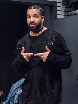 Drake poses in a black long-sleeved shirt with leather strap details, pointing both index fingers toward himself, seemingly confident amid sliding album-release odds. The image accompanies news that his Polymarket odds to drop an album by year-end fell from 80% to 42%.