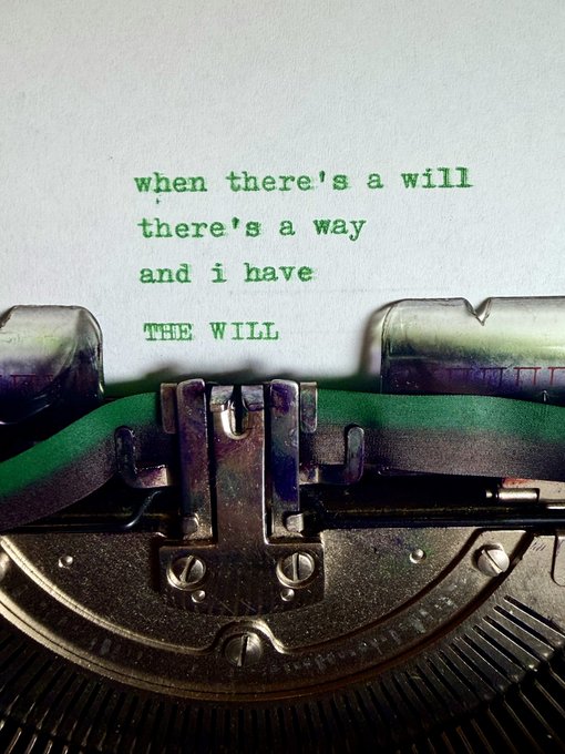 A close-up of a vintage typewriter with green-typed text on paper reading: 'when there's a will there's a way and i have THE WILL'.