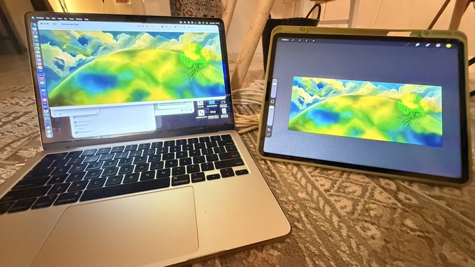 A MacBook laptop and a tablet sit side by side on a textured surface, both displaying what appears to be the same colorful 3D topographical or scientific visualization with green, yellow, and blue hues.