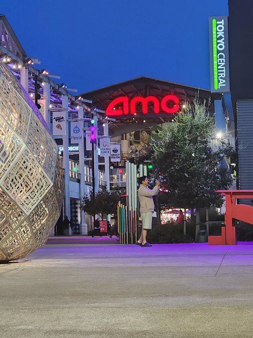 A person takes a photo of the Tokyo Central movie theater, featuring a large red and white sign with the word "AMC" on it.