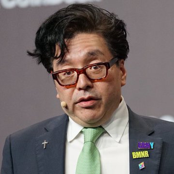 The image shows a man wearing glasses, a suit jacket, and a green tie. He has a serious expression as he looks directly at the camera. The background of the image is gray with some text visible that reads "BREAKING: BitMine just added another 111,942 $ETH in a single week. Company now holds 5.39 MILLION ETH, around 4.47% of Ethereum's total supply. Current breakdown: • 4.71M ETH already staked (~$10.1B)  + ORBS + $444M cash". The man appears to be discussing the recent addition of funds by Bit Mine and how it has affected their stake in the cryptocurrency market, specifically in the Ethereum network.