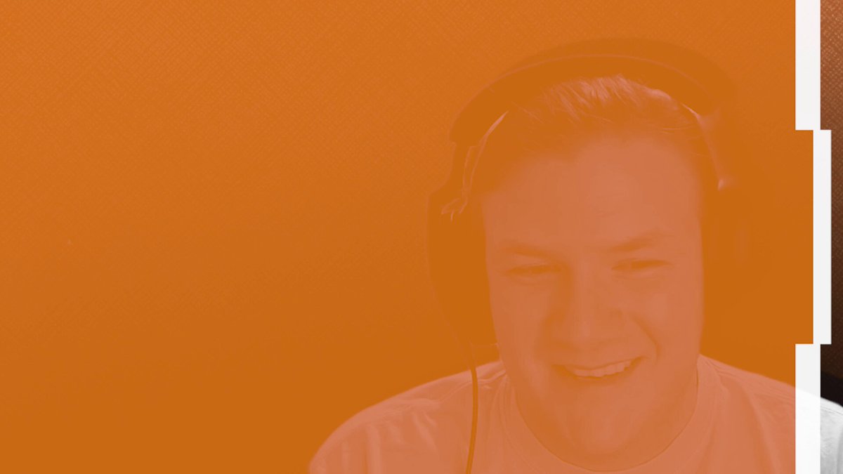 The image features a man wearing headphones, smiling at the camera with his tongue sticking out. The background of the photo has an orange hue that contrasts with the gray wall behind him. There are also other people visible in the image, but they are not the main focus and do not appear to be related to the main subject or the post on social media.