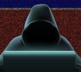 A shadowy hooded figure types on a laptop in front of a backdrop of red scrolling code, visually evoking a hacker or cybercriminal. The image relates to the post about Trezor reporting that 67,000 customers were affected by the ShipMonk data breach, symbolizing the online threat behind such cyber incidents.