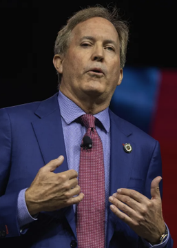 A middle-aged man in a blue suit and checkered tie speaks animatedly with his hands raised, set against a red, white, and blue backdrop, likely at a Republican political event. The image appears to illustrate Ken Paxton, whose Texas Senate race odds have reportedly dropped to 41% following leaked audio in which he allegedly blamed Trump's convention for declining GOP poll numbers.