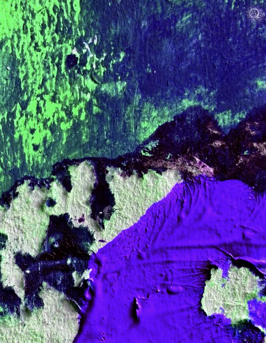 A false-color satellite image showing textured terrain in vibrant greens, dark blues, and bright purples, likely depicting vegetation, water, and land features.