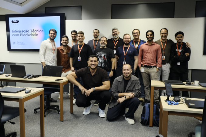 A group of approximately 17 participants poses together in a classroom setting, with a presentation screen displaying "Integração Técnica com Blockchain - Cardano Foundation." The image captures the team from the three-day workshop held in Recife with CESAR, featuring educators and researchers who gained hands-on experience with Cardano and heard from ecosystem partners like Blockforce and UNDP.