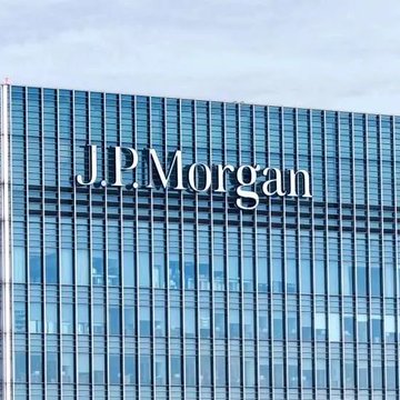 The image shows the exterior of a J.P. Morgan building featuring the bank's "J.P. Morgan" name displayed prominently on its modern glass facade. This visual ties directly to the post's news about J.P. Morgan warning that delays in passing the CLARITY Act would negatively impact crypto market growth, as the company weighs in on U.S. cryptocurrency regulation.