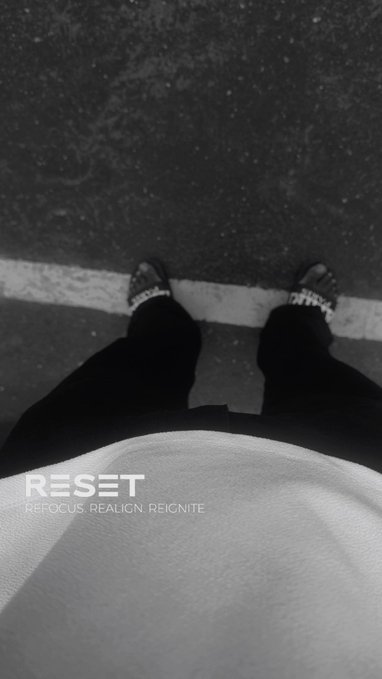 A black and white photo looking down at a person's feet wearing sandals, featuring the text 'RESET: REFOCUS. REALIGN. REIGNITE.'