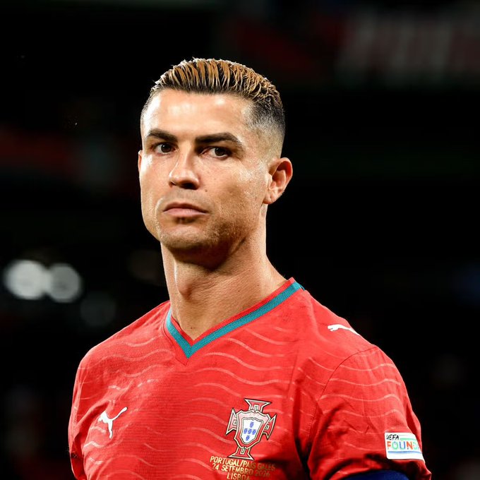 A focused Cristiano Ronaldo, wearing Portugal's red Puma jersey with the federation crest and UEFA "Equal Game" patch, is shown prior to a match. The image ties to the post's discussion of Ronaldo being left out of the Portugal squad for an upcoming UEFA Nations League fixture against Denmark.