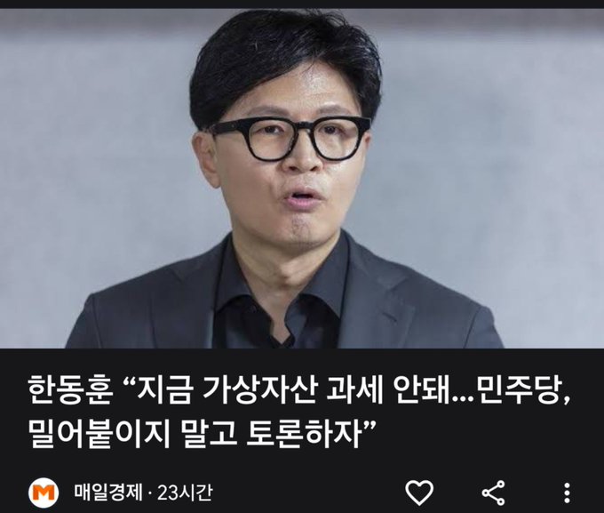 The image shows a screenshot from the Korean news outlet "매일경제" (Maeil Business Newspaper), published 23 hours ago, featuring a close-up photo of Han Dong-hoon, a South Korean politician, wearing glasses and a dark suit while speaking. The accompanying headline reads: "한동훈 '지금 가상자산 과세 안돼…민주당, 밀어붙이지 말고 토론하자'" which translates to his call for the Democratic Party to debate rather than push through the cryptocurrency taxation issue, arguing it's not appropriate to tax virtual assets at this time—aligning with the post's description of him urging a deferral of the crypto tax.
