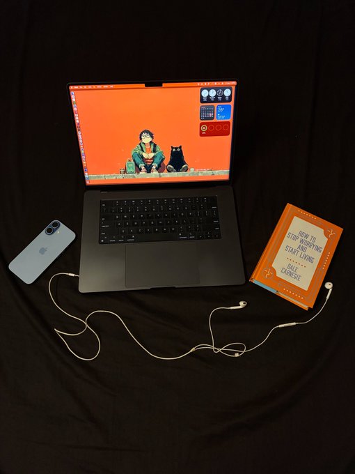 A flat-lay photo on a black background shows a laptop with an orange wallpaper featuring two figures, an iPhone, white earphones, and an orange book titled "HOW TO STOP WORRYING AND START LIVING" by Dale Carnegie.